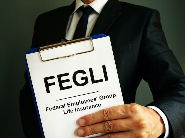 Close up of a businessman's hand holding a clipboard that reads 'FEGLI - Federal Employees Group Life Insurance'