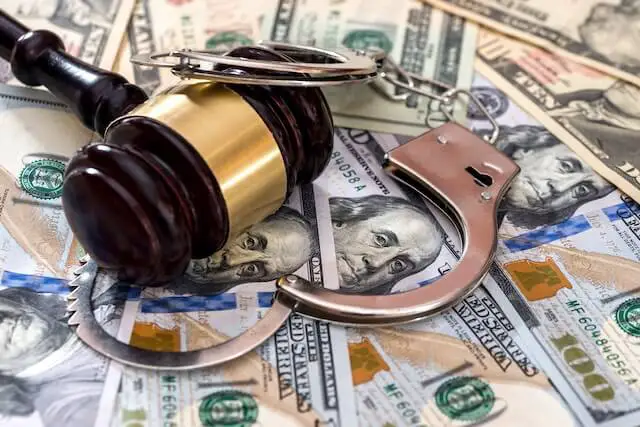 Wooden judge's gavel and a pair of handcuffs lying on top of a spread of $100 bills