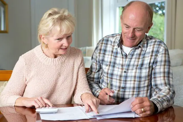 Senior aged couple studying paperwork at a table with a calculator