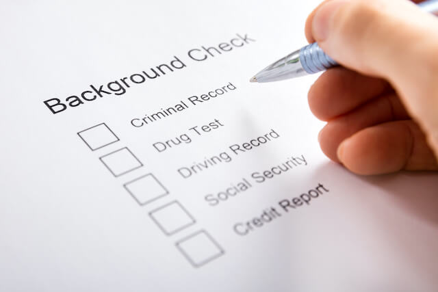 Close up of a person's hand holding a pen filling out a form labeled 'background check' with 6 checkboxes on it