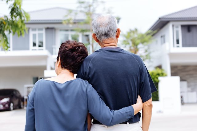 Happy senior aged couple seeing from behind embracing as they look at the front of their home