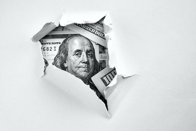 Hole in paper being torn back revealing the face of Benjamin Franklin on a $100 bill