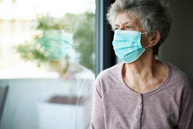 Senior citizen aged woman wearing a face mask as she looks out of a window