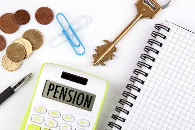 Word 'pension' displayed on a calculator's screen sitting on a desk next to coins, paperclips, a key, pen and notepad