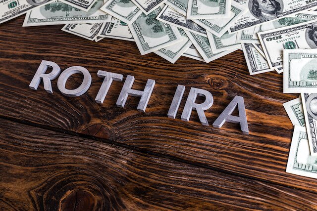 Words 'Roth IRA' pictured on a wooden surface surround by a spread of cash