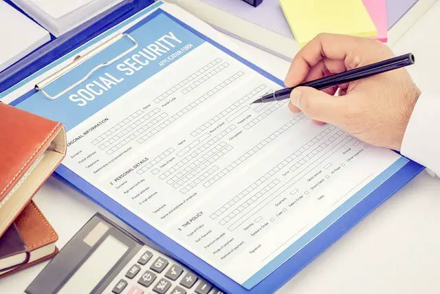 Close up of a person filling out a social security application; a calculator is pictured next to the form