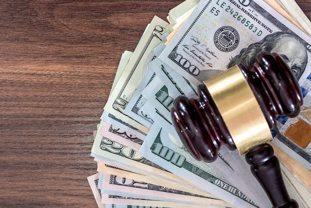 Wooden judge's gavel sitting on top of a spread of cash on a wooden surface