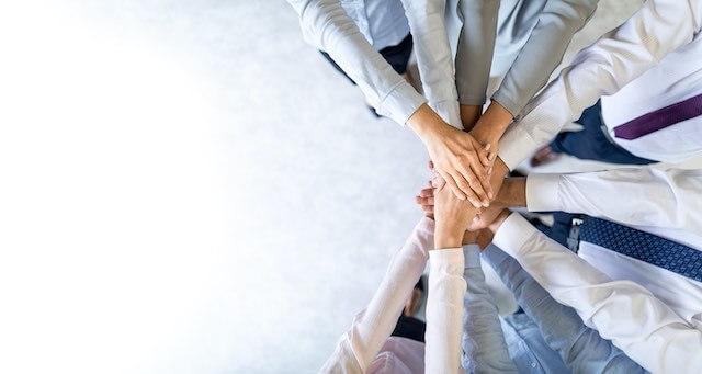 Close up of the hands of a group of employees placed in a circle on top of one another in a show of collaboration/teamwork/unity