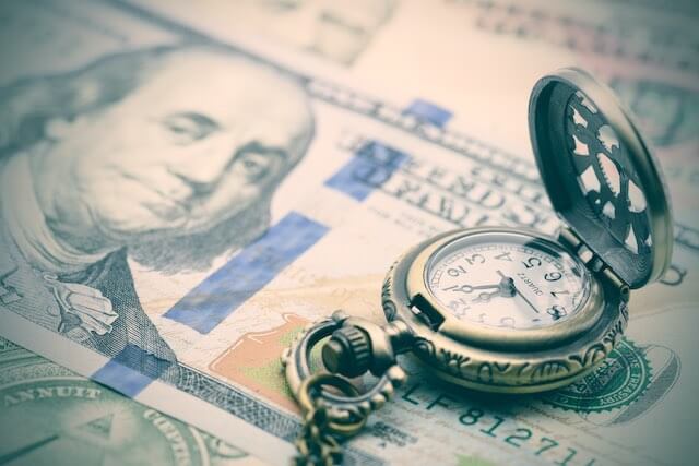 Face of a $100 bill with an old style pocket watch sitting on top of it