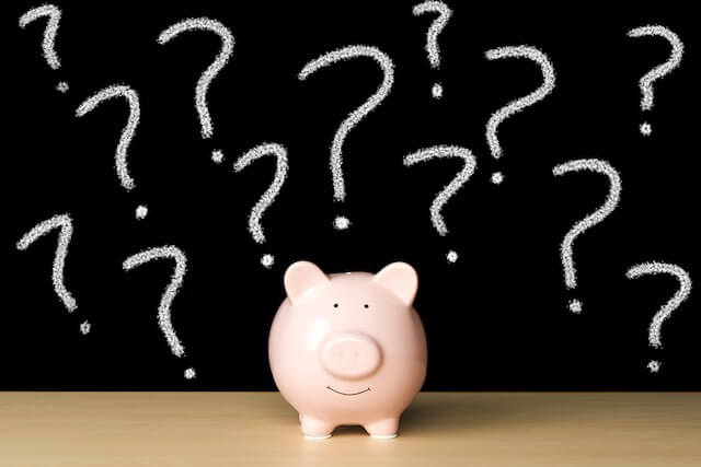 Pink piggy bank on a wooden surface with question marks drawn on a chalkboard behind it