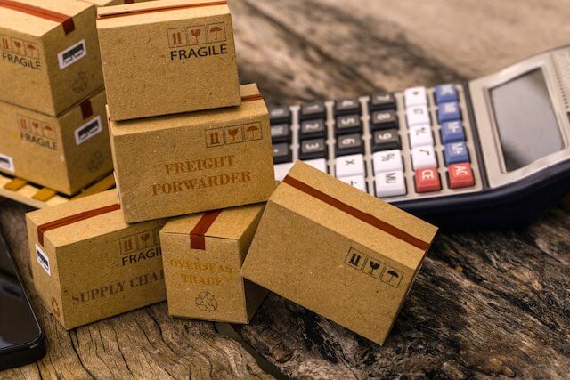 Commercial shipping boxes in a stack next to a calculator on a wooden surface