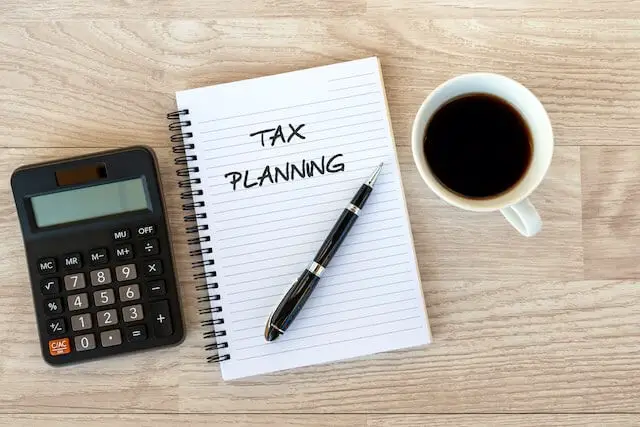 Words 'tax planning' written on a notepad next to a calculator and cup of coffee sitting on a wooden surface