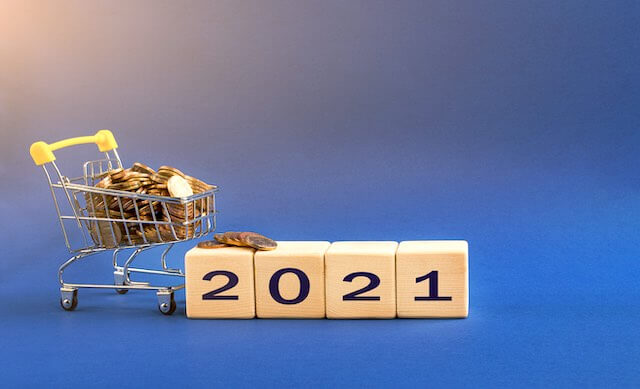 Mini shopping cart filled with coins next to wooden blocks that read '2021'