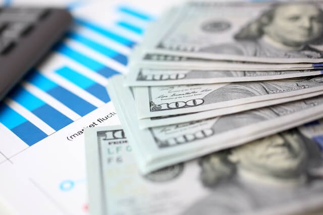 Spread of $100 bills in cash on top of a financial document with a bar chart visible and a calculator seen off to the side