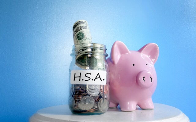 pink piggy bank next to a glass jar with money in it labeled 'HSA'