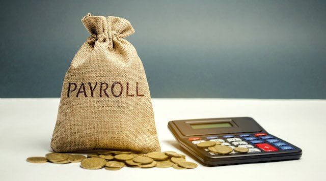 Burlap bag labeled 'payroll' with coins around it and a calculator sitting next to it