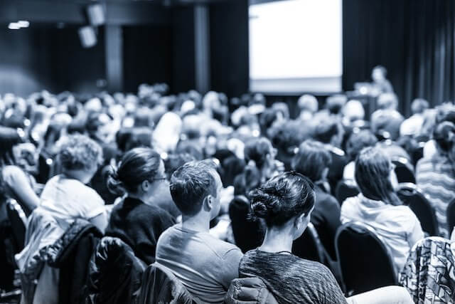 Group of attendees listening to a speaker giving a presentation in an auditorium