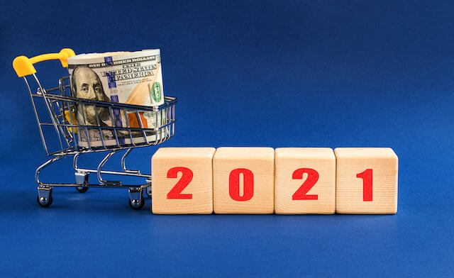 Roll of cash in a small shopping cart next to wooden block letters that read '2021'