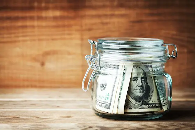 Dollar bills in jar on rustic table. Saving money concept.
