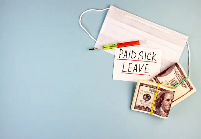 Face mask, thermometer, and cash on a solid blue surface next to a note that says 'paid sick leave'