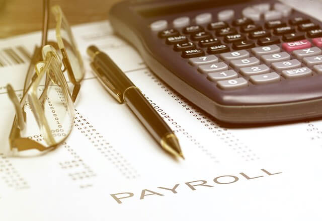 Glasses, a pen and calculator sitting on top of a financial worksheet labeled 'payroll'