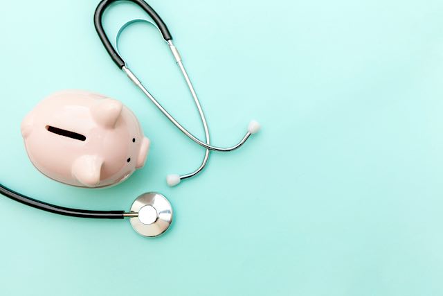 Pink piggy bank pictured next to a stethoscope on a solid aqua colored background