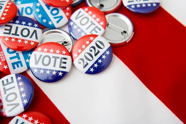 Pin on buttons spread on the backdrop of an American flag that say 'vote' and '2020'