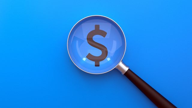 Magnifying glass centered over a dollar sign against a blue background