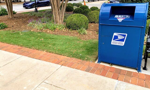 Blue Postal Service (USPS) mailbox on a city sidewalk