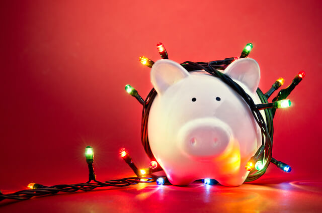 Piggy bank wrapped in Christmas string lights against a red background
