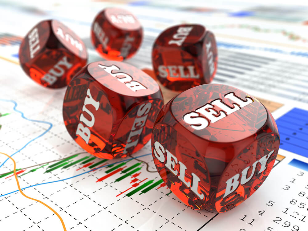 Red dice that read 'buy' and 'sell' pictured on top of financial charts and graphs