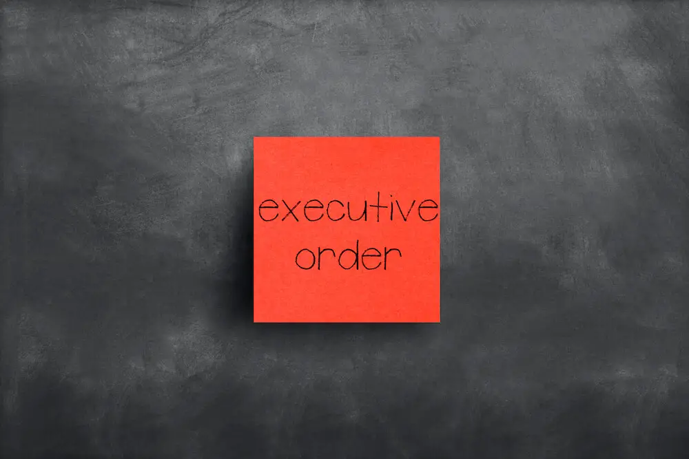 Words 'executive order' written on a red sticky note attached to a blackboard