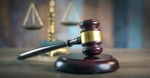 Wooden judge's gavel on a desk with a blurred view of justice scales in the background