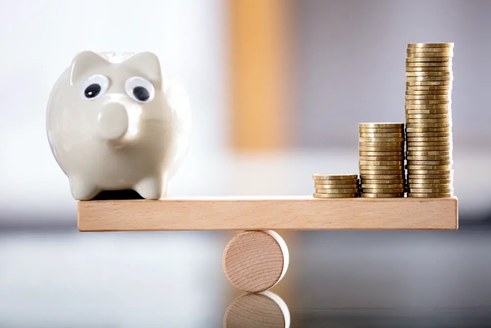 Evenly balanced seesaw with a piggy bank on the left side and 3 vertical stacks of coins on the right side