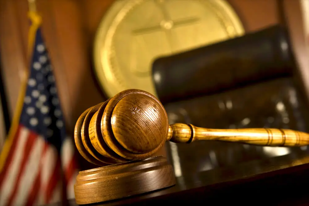 Wooden judge's gavel with an American flag and a judge's chair pictured in the background