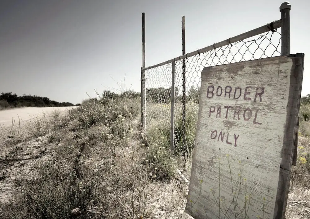 Sign reading 'Border Patrol Only' in front of a section of chain link fence along the southern border