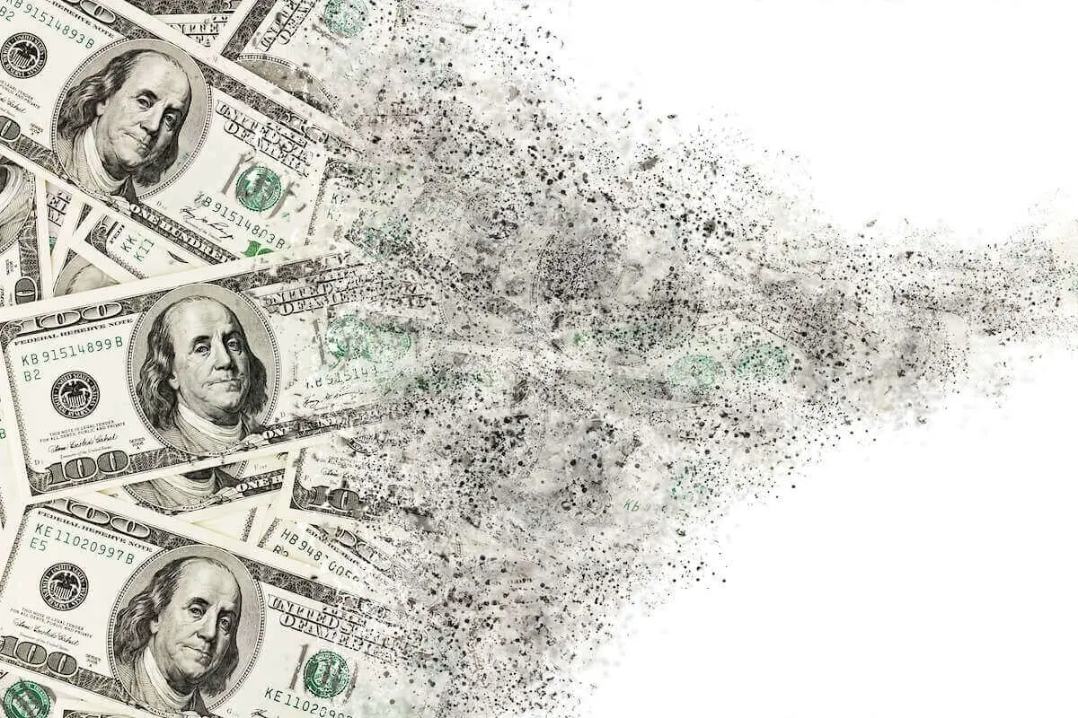 Spread of hundred dollar bills disintegrating against a solid white background