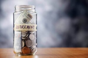 Glass jar of coins and cash labeled 'retirement' depicting retirement savings