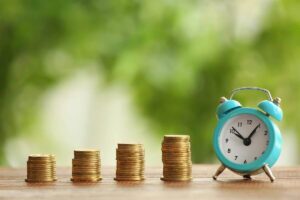 Four vertical stacks of coins growing in height from left to right next to an old style alarm clock