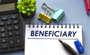 'beneficiary' written on a notepad next to a calculator and paper clips on a desk work area