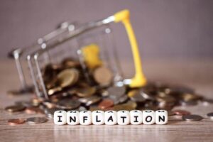 Tipped over shopping cart with coins scattered around it with the word 'inflation' written in block letters in the foreground
