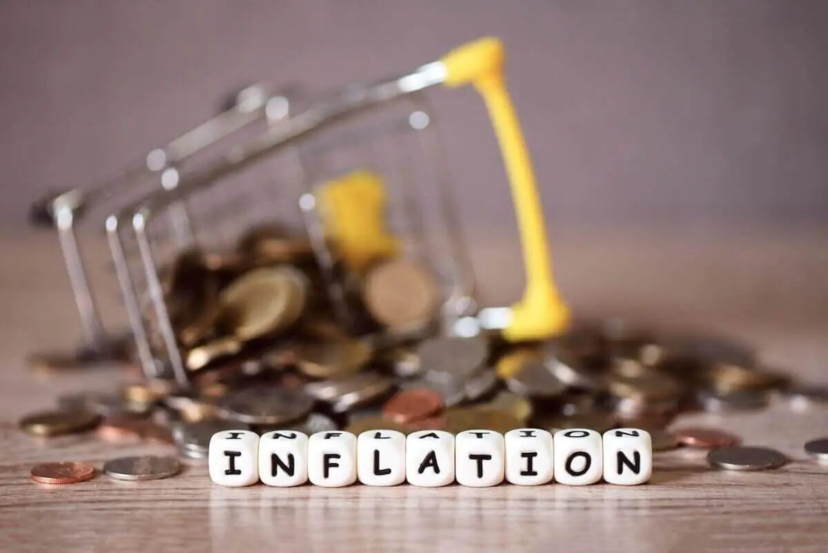 Tipped over shopping cart with coins scattered around it with the word 'inflation' written in block letters in the foreground