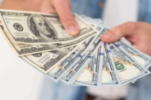 Close up of a person's hands holding hundred dollar bills in a fan shape