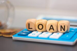 Block letters spelling the word 'loan' sitting on top of a calculator next to a jar of money