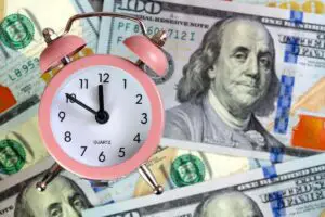 Old style alarm clock on top of a spread of $100 bills