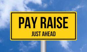 Yellow sign that reads 'pay raise just ahead' against a blue sky background