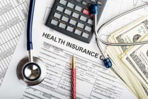 Health insurance paperwork with a stethoscope, calculator, pen and spread of cash