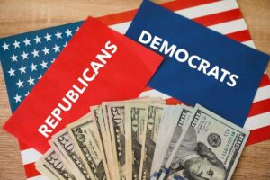 Spread of cash over two cards, one red that reads 'Republicans', the other blue and reads 'Democrats'; both are on top of a US flag