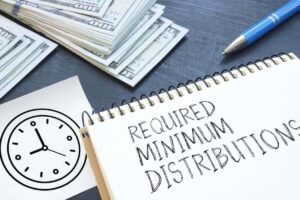 Notepad on a desk with words 'required minimum distributions' written on it; a pen, sketch of a watch, and stack of cash is lying next to it
