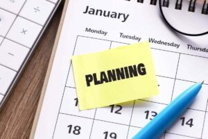 Calendar for January with a post it note stuck on it that reads 'planning'; pen and eyeglasses are lying next to it